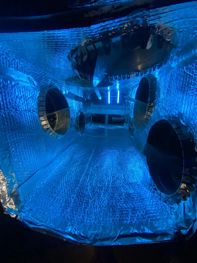 Plenum box repair: blue-lit interior of a foil-lined plenum showing sealed duct collars and openings