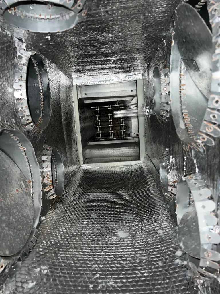 Plenum box repair: view down a metal plenum interior toward the unit, collars fastened along the walls