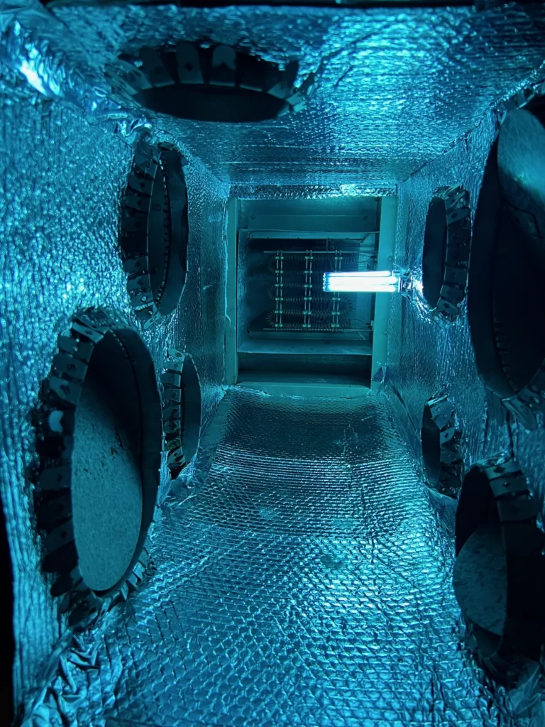 Plenum box repair: UV light glowing inside a foil-lined plenum with sealed round duct openings