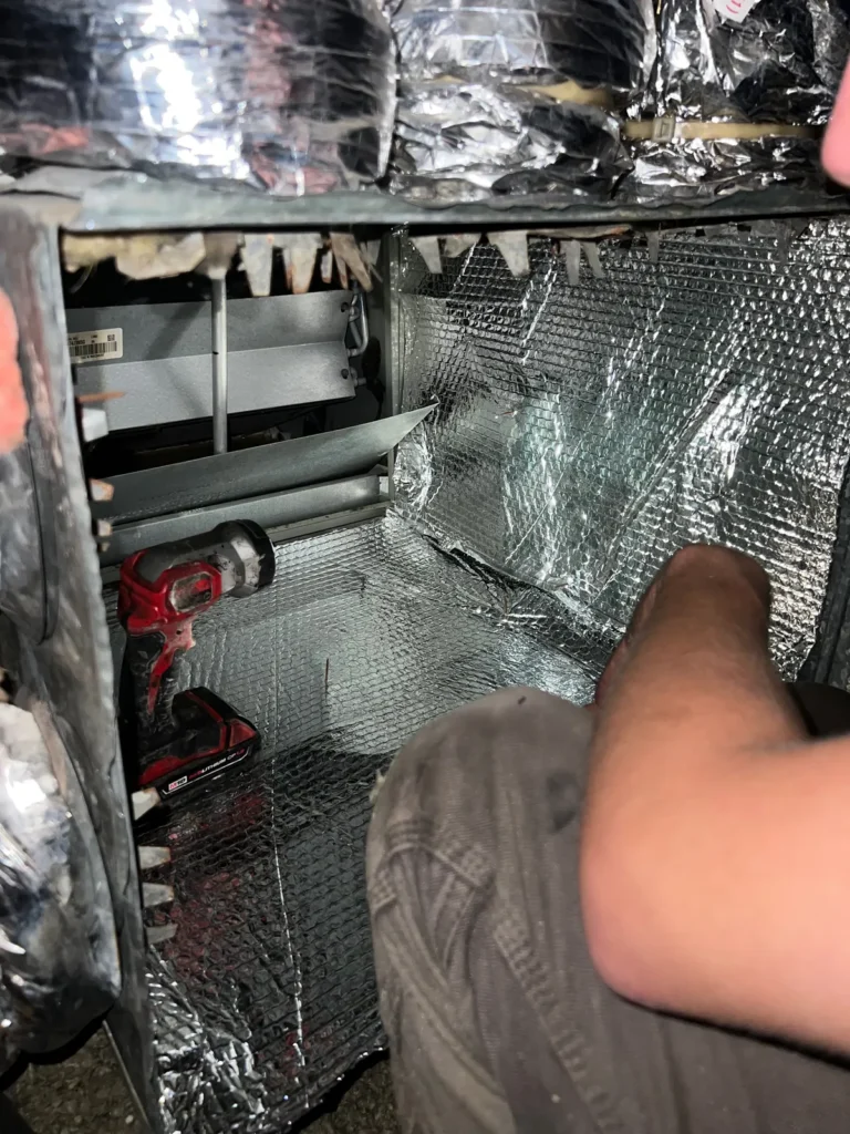Plenum box repair: technician working inside an open plenum with a cordless drill and new foil lining