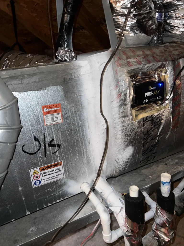 UV light installation: unit and UV warning labels on a foil-wrapped air handler in an attic